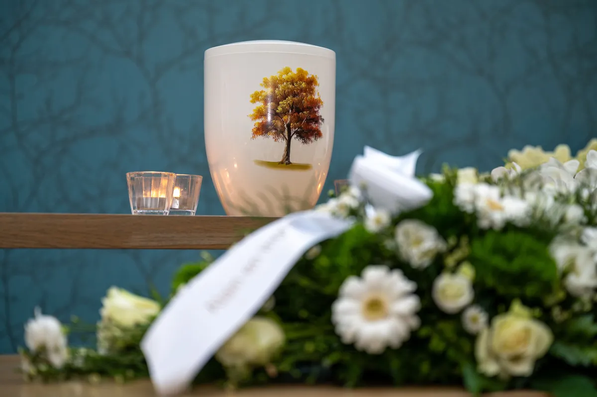 Witte urne met een geschilderde boom, brandende kaarsjes en witte bloemen met een lint